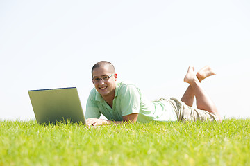 Image showing A young men lying on the in the park using a laptop