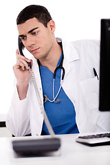 Image showing Caucasian male doctor sitting at the desk with computer talking over phone