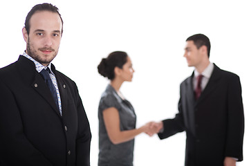 Image showing Handsome business man looking at us, two collegues giving shakehand at the background