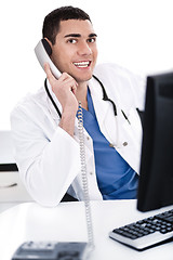 Image showing Smiling young physician sitting at his desk talking over phone