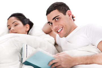 Image showing Woman sleeping and man happily reading book in bed