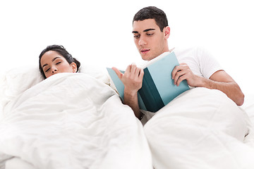 Image showing Young handsome man reading book while is wife sleeping beside him in bed