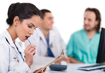 Image showing Young asian doctor thinking with the pen, others blurred behind