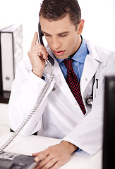 Image showing young physician sitting at his desk talking over phone