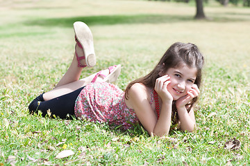 Image showing happy cute girl  laying on a grass field and looking stright