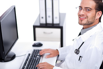 Image showing Smiling young doctor working on his desk