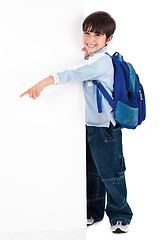 Image showing Young kid happily standing behind the board and pointing to empty space