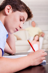 Image showing Young teenager writing in his notebook in living room