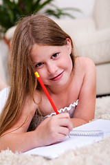 Image showing Smiling young girl lying and writing in notebook