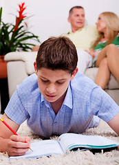 Image showing Young boy studying with family in the background