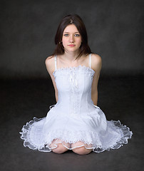 Image showing Girl in a white dress sits on a black background