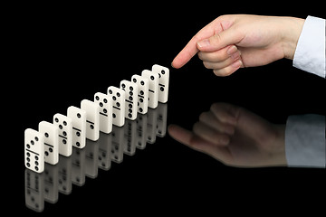 Image showing Hand pushing dominoes counters on black