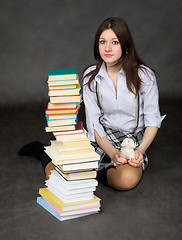 Image showing The beautiful schoolgirl sits near a pile of books