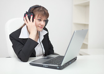 Image showing Woman in ear-phones sits with laptop at table at office