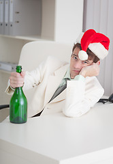 Image showing Young businessman in Christmas cap sits with bottle at table