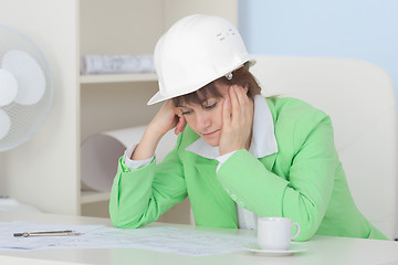 Image showing Woman - engineer in protective helmet sits at table on workplace