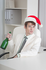 Image showing Young man in Christmas cap sits with bottle at table