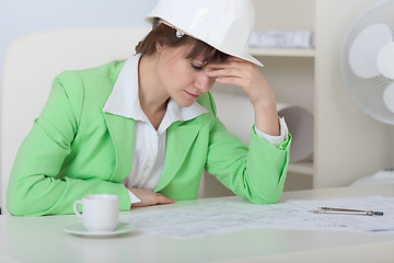 Image showing Tired woman - engineer in helmet sits at table in office