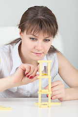 Image showing Young girl builds tower of dominoes bones on table