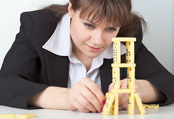 Image showing Young girl in black concentrated builds tower of dominoes