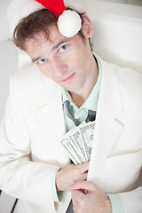 Image showing Businessman in white suit and Christmas cap hides money in pocke