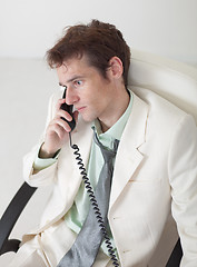 Image showing Man in white suit speaks by phone sitting in an armchair