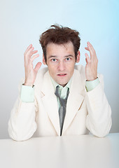 Image showing Young sorrowful man in white suit sits at table