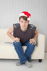 Image showing Guy in Christmas cap sits on sofa having stare wide-eyed