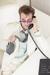 Image showing Young businessman speaks on phone, worries and rumples tie