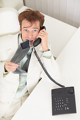 Image showing Young businessman speaks on phone, worries and bites tie