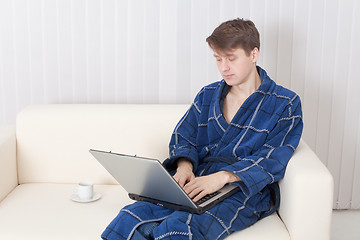 Image showing Young man works with laptop in blue dressing gown