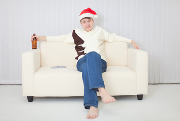 Image showing Person in a Christmas cap comfortably sits on sofa with beer