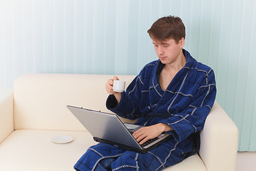 Image showing Guy works in Internet on sofa and drinks coffee