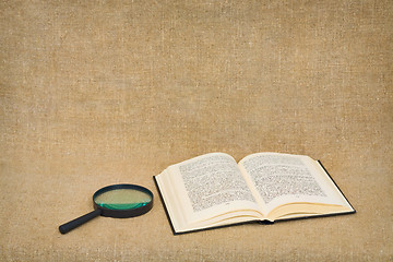 Image showing Magnifier and open book lie against a brown canvas