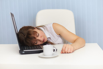 Image showing Young woman sleeps on laptop keyboard on workplace