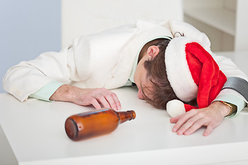 Image showing Drunk person in a Christmas cap lies on white table