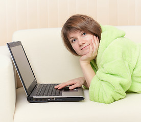 Image showing Young woman in green dressing gown on sofa with laptop