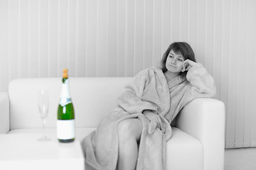 Image showing Lonely young woman sits on sofa and looks at wine bottle