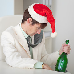 Image showing Drunk man in a Christmas cap with bottle sits at table