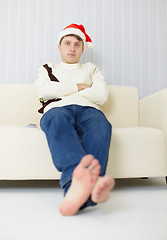 Image showing Person in a Christmas cap sits on sofa and watches TV