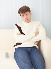 Image showing Serious guy sits on sofa with remote control