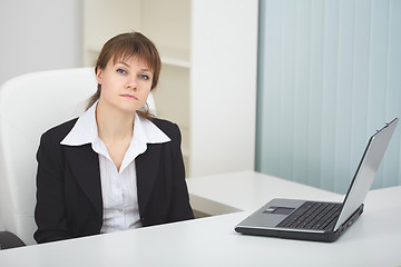 Image showing Serious woman sits at table at light office with laptop