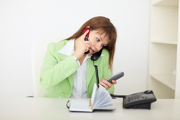Image showing Beautiful woman - secretary speaks by several phones simultaneou