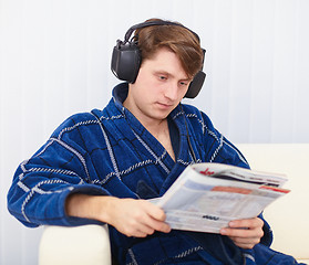 Image showing Man in big ear-phones on sofa reads newspaper