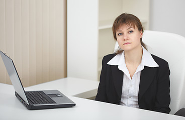 Image showing Serious woman sits at table at light office with laptop