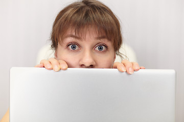 Image showing Amusing girl hides behind laptop screen