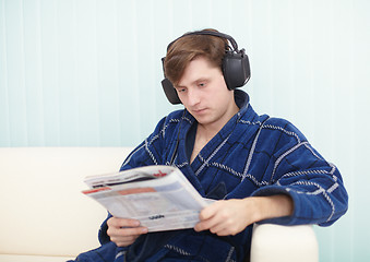 Image showing Person in big ear-phones on sofa reads newspaper