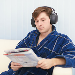 Image showing Man in big ear-phones on sofa reads newspaper