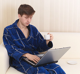 Image showing Guy works in Internet on sofa and drinks coffee