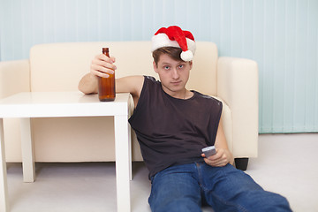 Image showing Young man in christmas hat sits on a floor with beer